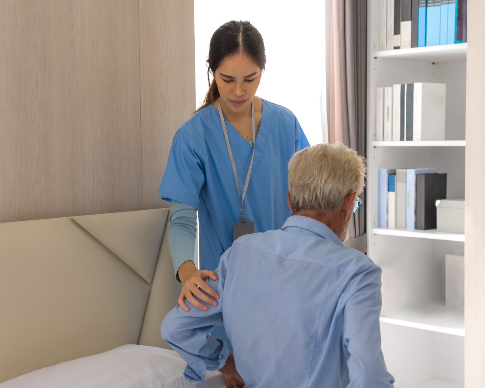 A SteadiCare caregiver helping an older man up at his bedside