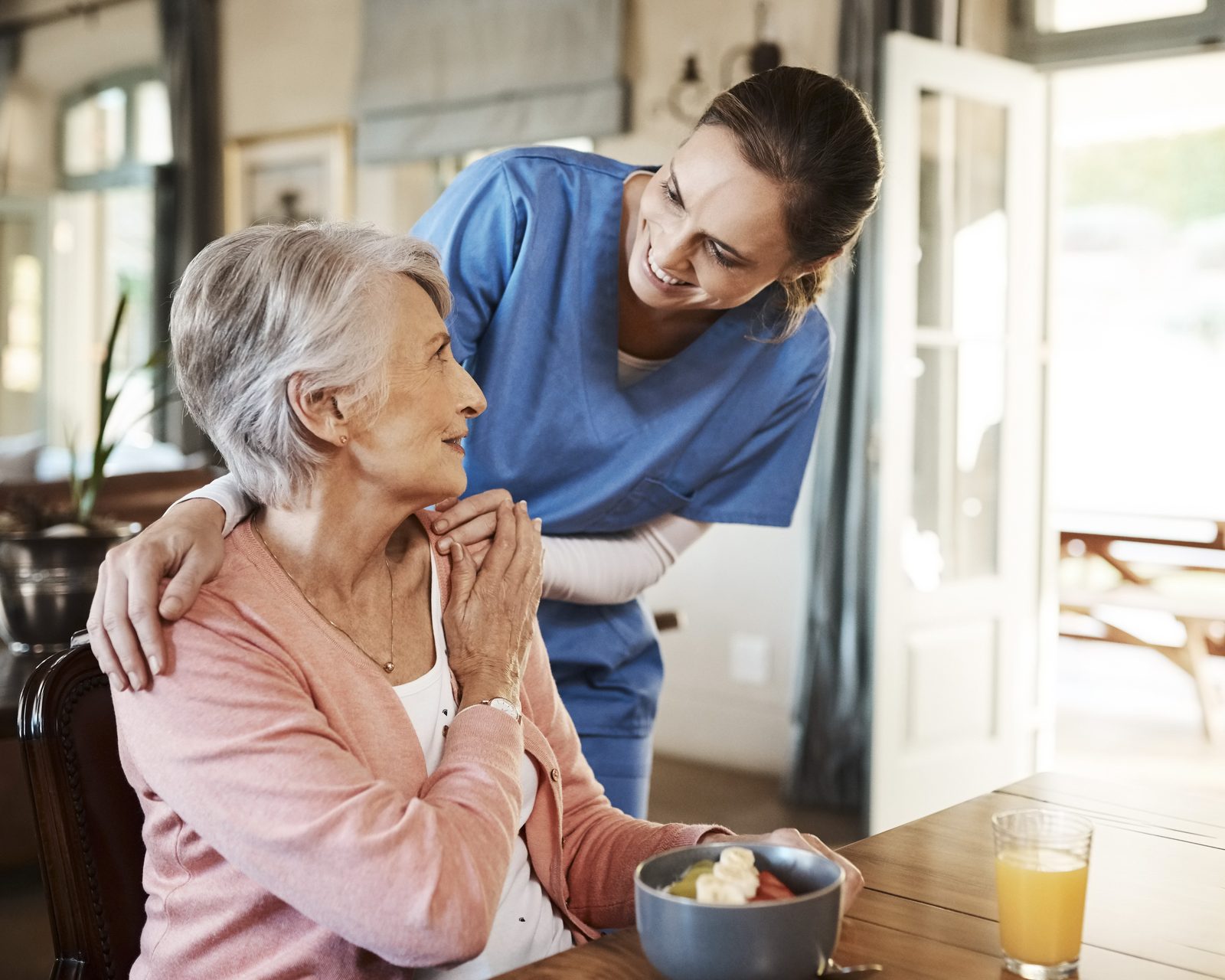 A SteadiCare caregiver warmly attending to a senior woman at her breakfast table